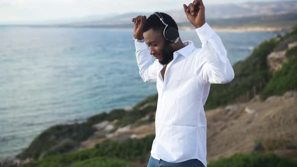 Cheerful African American Gay Man in Headphones Dancing in Slow Motion on Mediterranean Sea Coast