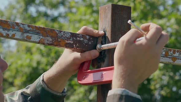 Slow Motion Closeup Man Fixes Metal Plank with Clamp in Yard