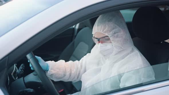 Unidentifiable Person in Protective Overall Suit Driving Car