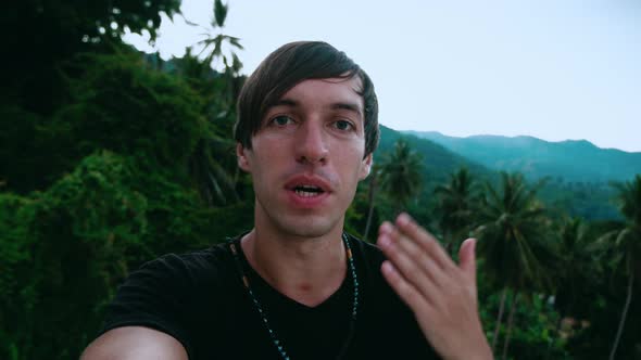 Smiling Young Man Tourist Making a Selfie or Video Call on Green Jungle Forest Background