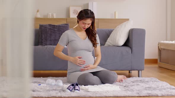 Happy Pregnant Woman sit on carpet holding stroking her big belly with diaper