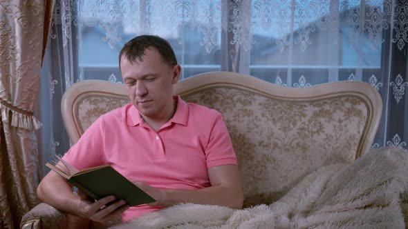 Attractive Man Reading a Book While Sitting in the Evening on the Sofa