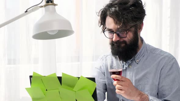 Man Types and Enhoy a Glass of Wine and Looks Happily at the Computer Screen