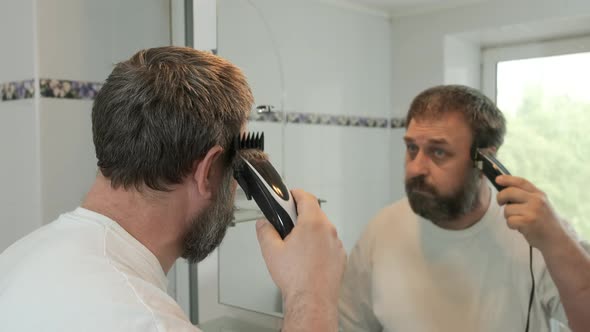 A man cuts himself with an electric hair clipper in the bathroom. Adaptation to souial distance. 