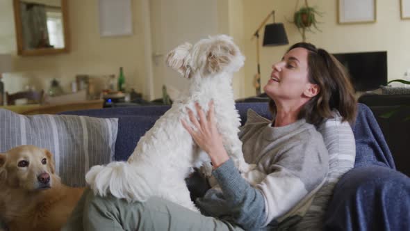 Smiling caucasian woman kissing and cuddling her pet dog sitting on sofa at home