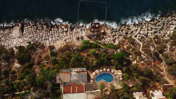 Top View of a Coastal Resort with Lounge Zone and Swimming Pool Located in Front of Rocky Beach