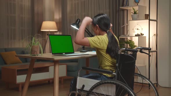 Asian Kid Girl Sitting In A Wheelchair While Using Laptop Green Screen And Celebrating At Home
