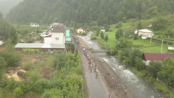 Drone shot of a cycling race in rural Romania on a wet road nearby a gushing river on a misty summer