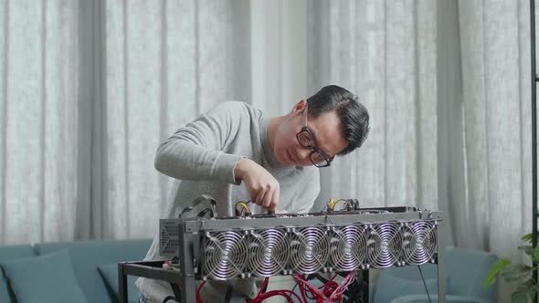Asian Man Wearing Glasses Connects The Power Cords Of Mining Rig For Mining Cryptocurrency