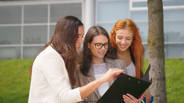 Business Women Browse the Contents of Documents in a Black Folder and Have Fun Laughing. Cheerful