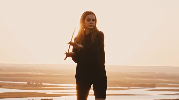 Young Woman Training with Swords on the Hill While Sunset  Midges Flying Around