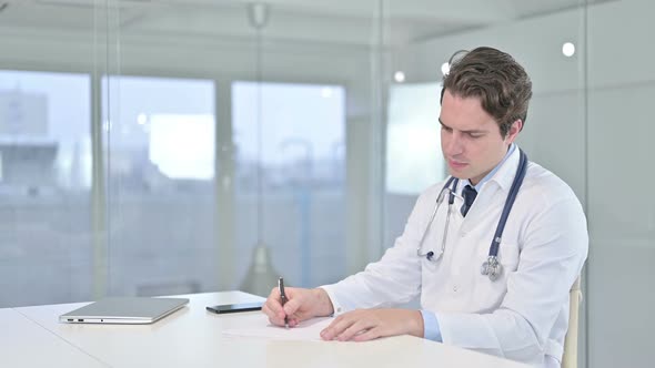 Serious Young Doctor Doing Paperwork in Modern Office 