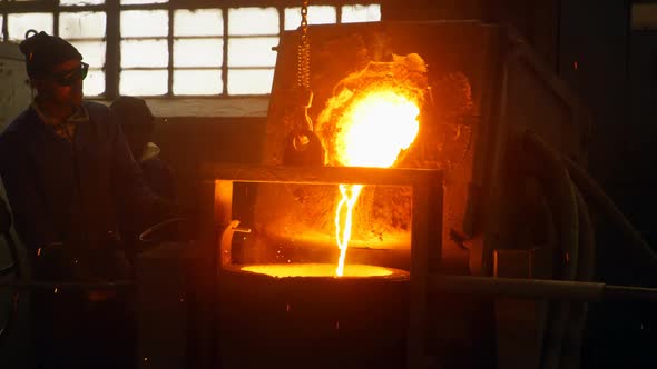 Worker pouring molten metal from container in foundry workshop 4k