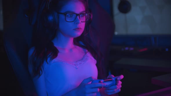Young Pretty Woman in Glasses Playing Online Games in Modern Neon Gaming Club and Chewing a Bubble