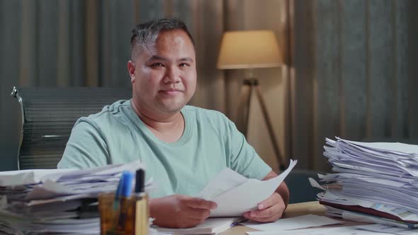 Close Up Of Fat Asian Man Smiling To Camera While Working With Documents At The Office