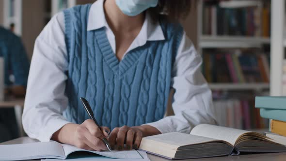 Closeup Unrecognizable Young Woman in Medical Protective Mask Sitting at Desk in Library Unknown