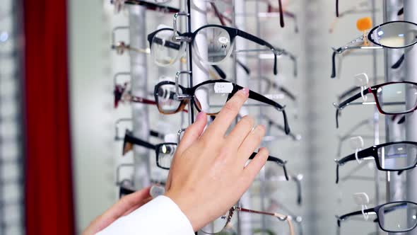 Eye glasses on the shelf. Young woman buying new glasses at optician store