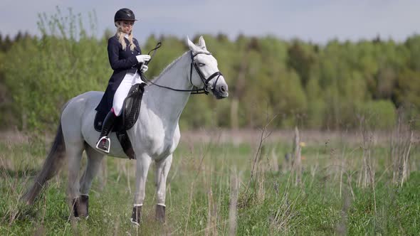 A Female Jockey Poses in a Field Riding a Horse