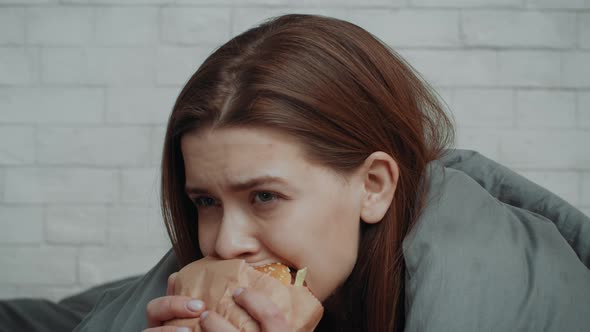 Depressed Young Woman Eating Burger To Comfort Herself At Home