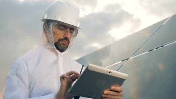 Man in Protection Wear Is Operating a Tablet Next To a Massive Solar Installation