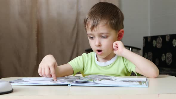 A Child Reads a Book While Sitting at the Table at Home