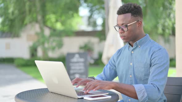 African Man Working on Laptop in Outdoor Cafe