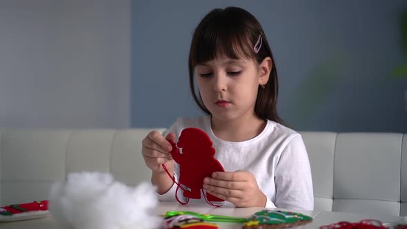 Child Girl Sews Textile Felt Santa for Christmas Tree Decoration