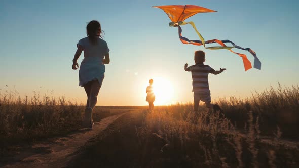 Happy Young Mother with a Children Play Kites Together on Park