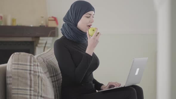 Young Muslim Woman Was Working or Chatting By Laptop and Biting Juicy Apple Wearing Traditional