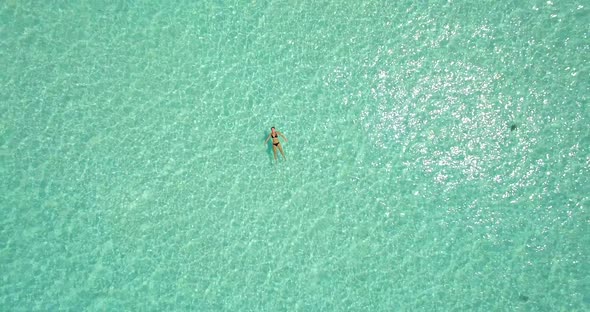Aerial drone view of a woman floating and swimming on a tropical island.
