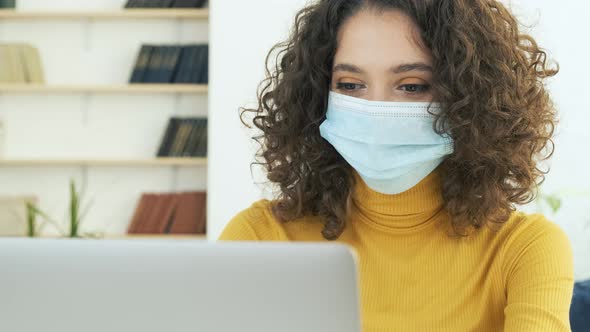 Young Business Woman in a Medical Protective Mask Works From Home at the Computer During