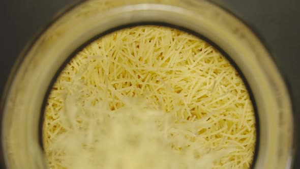 Uncooked Filini Pasta Falls Into Glass Jar On Black Background