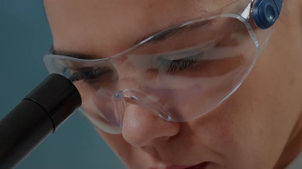 Woman Chemist with Protective Glasses Using Microscope