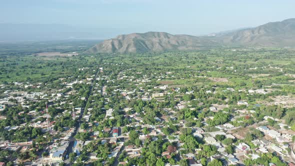 Aerial view over rural city of Neiba during sunny day and stunning mountain range in background - Ba