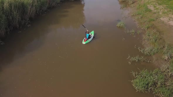 Man kayaking on meandering river, drone follows and pans up to reveal beautiful landscape in the bac