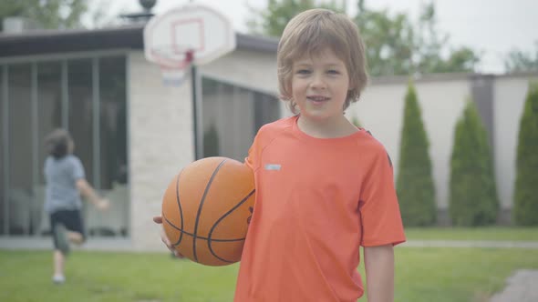 Little Boy Looking at Camera and Smiling As Blurred Kid Playing Basketball at the Background