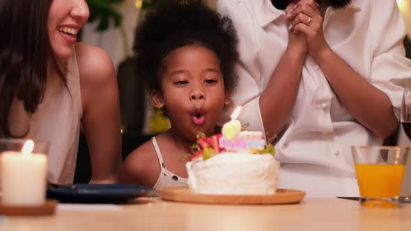 Happy little girl celebrating her birthday with Lgbt family blowing out the candles