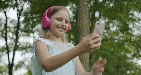 Happy Girl Communicate Online Video Call with Modern Pink Headphones in Park