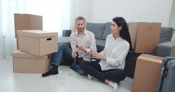 Moving To a New Apartment, a Young Couple Sitting on the Floor Near Boxes of Things and Drinking