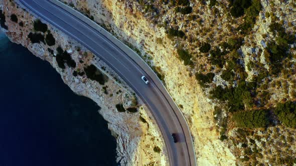 Aerial View of White Car Driving on Country Road Near Sea and Mountains