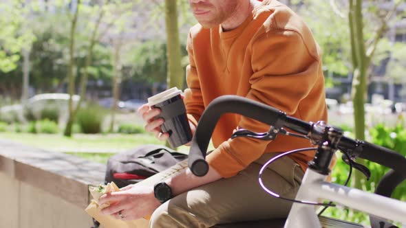 Albino african american man with dreadlocks sitting in park with bike drinking coffee