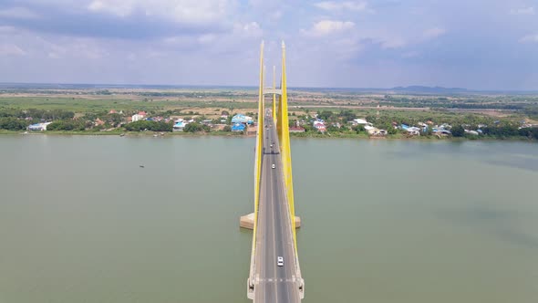 Aerial flyover Neak Loeung Bridge with driving cars crossing calm Mekong River during sunny day. Rur