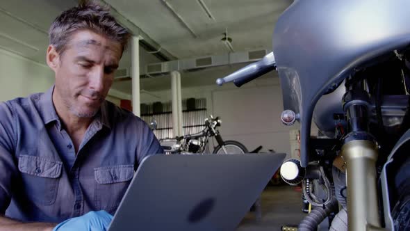 Male mechanic using laptop in motorbike repair garage 4k