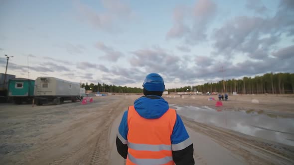 A Man in an Orange Protective Vest Walks Through an Oil Field