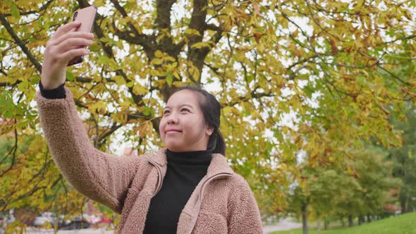 Happy Asian woman taking a selfie on smartphone at the park in Autumn