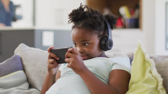 Happy african american girl lying on sofa using smartphone