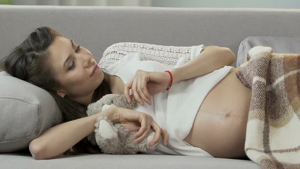 Expecting Female Lying on Couch With Teddy Bear, Putting Hand on Belly, Napping