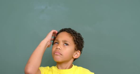 Front view of thoughtful African American schoolboy standing against chalkboard in classroom 4k