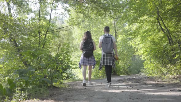 Portrait of Guy and Young Cute Girl Walking in the Forest. Pair of Travelers with Backpacks Outdoors