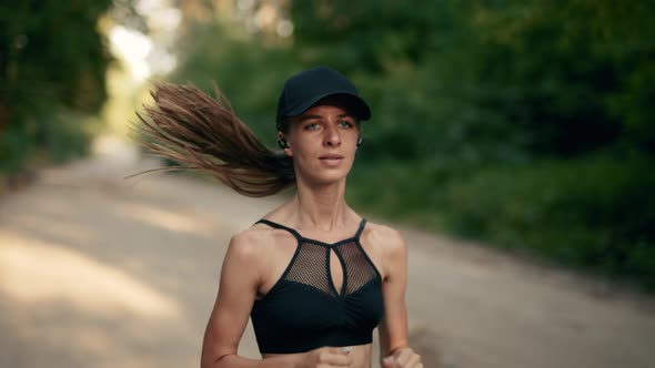 A Young Woman Runner is Listening to Music in Earphones and Training in Summer Forest